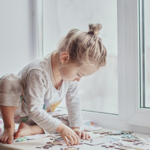 little girl collects puzzles by the window in light-colored hom